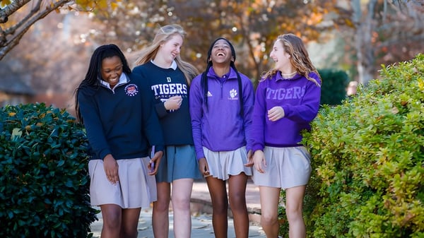 Cuatro estudiantes de la Darlington School están juntas al aire libre frente a árboles y hojas.