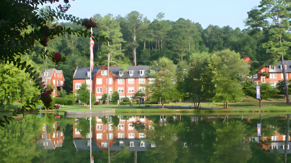 Un estanque en el terreno de la Darlington School refleja los edificios de ladrillo rojo y el paisaje forestal verde circundante.