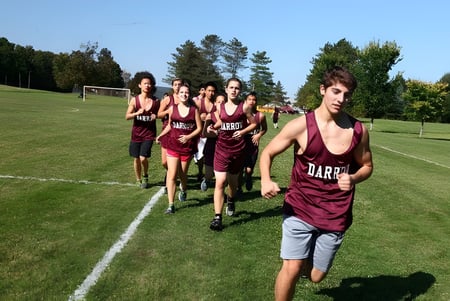Un grupo de estudiantes de la Darrow School camina por un campo deportivo con árboles al fondo.