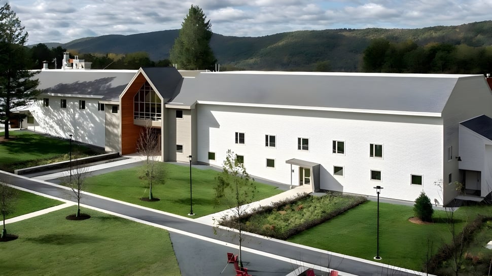 El moderno edificio blanco de la Darrow School con un arco destacado en un entorno cuidado y colinas verdes al fondo.