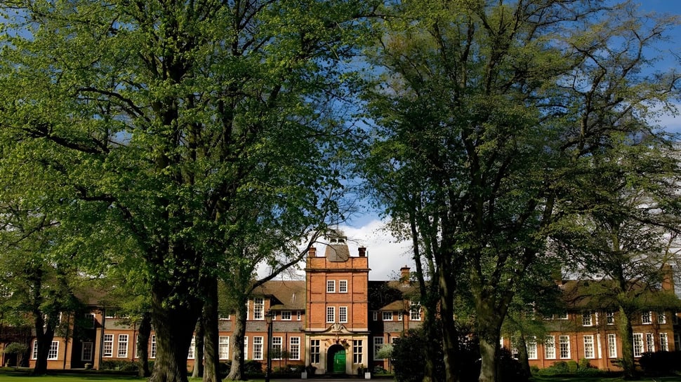 Edificio histórico de ladrillo de la Dauntsey’s School rodeado de árboles verdes bajo un cielo azul.
