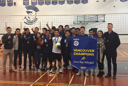 El equipo de voleibol de la David Thompson Secondary School posa en el gimnasio con un banner de campeonato.