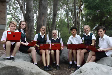 Estudiantes de la Davidson High School están sentados en uniformes escolares sobre rocas en un entorno boscoso.