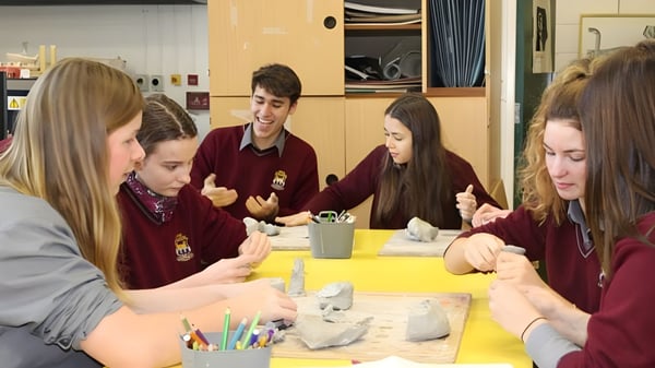 Estudiantes del Davis College trabajan juntos en un proyecto de arte con diferentes materiales en una mesa.