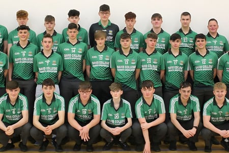 Un grupo de jóvenes atletas en camisetas verdes posan en el campus del Davis College frente a un fondo blanco.