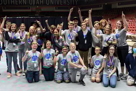 Un grupo de alumnas y alumnos del Davis School District posan juntos en un gran salón con una pancarta de la Southern Utah University de fondo.