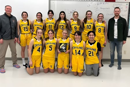 Un grupo de jóvenes jugadoras de baloncesto en camisetas amarillas posan junto a sus entrenadores en la Daysland School.