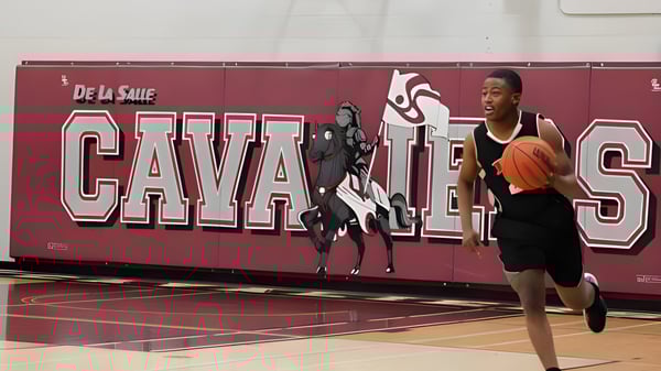 Un deportista está en la cancha de baloncesto con un gran mural de De La Salle Cavaliers de fondo en el campus de la École secondaire publique De La Salle.