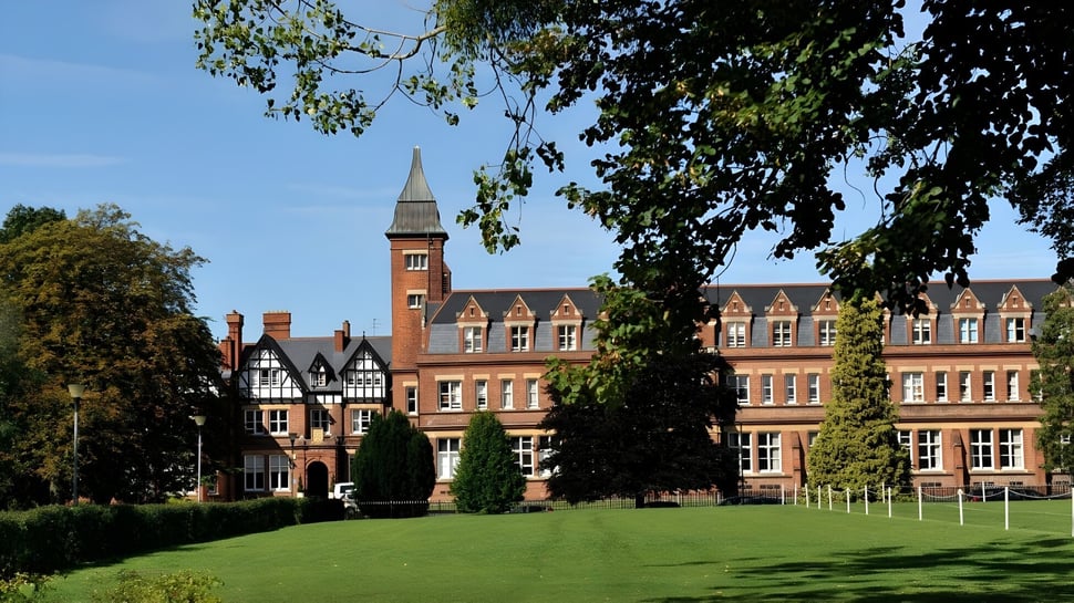 El edificio histórico de ladrillo en el campus verde de la Dean Close School con césped cuidado en primer plano.