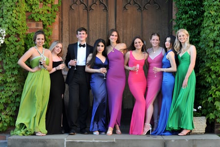 Un grupo de personas elegantemente vestidas posan juntas frente a una puerta de madera rodeada de plantas verdes en el terreno de la Dean Close School.