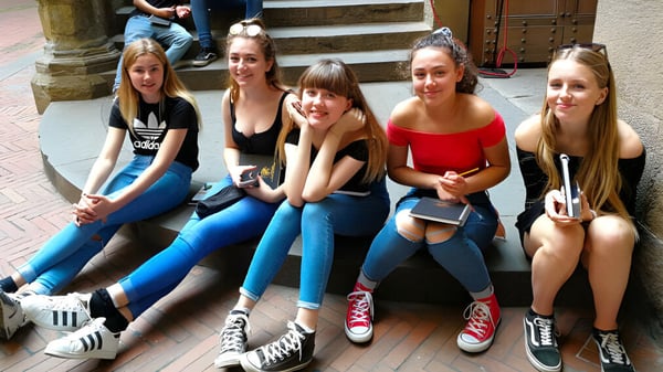 Un grupo de alumnas está sentada en los escalones de un edificio en el campus de la Denefield School y conversan entre ellas.