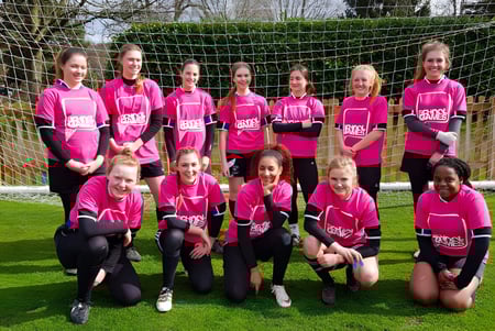 Un grupo de jóvenes futbolistas en camisetas rosas juega en el campo deportivo de la Denefield School.