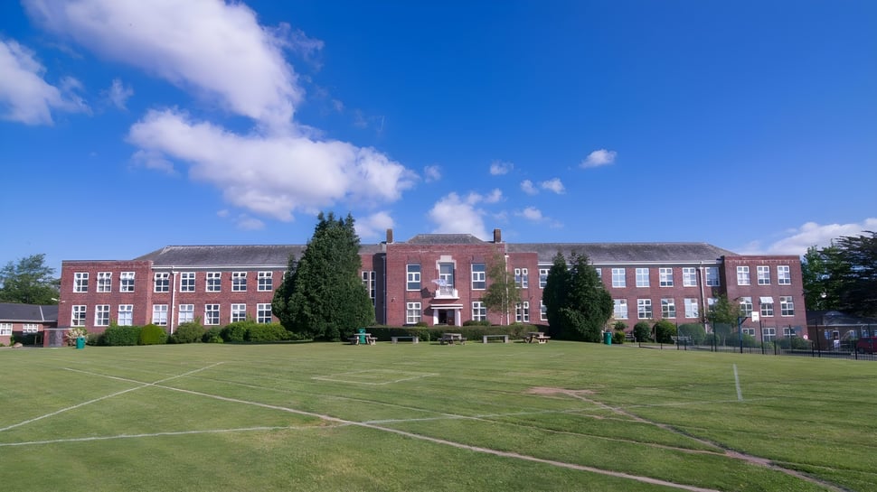 El gran edificio de ladrillo de la Devonport High School con una pradera en primer plano bajo un cielo azul.