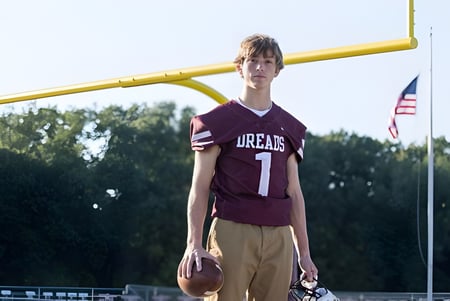 Un estudiante de la Dexter High School está frente a una portería de fútbol amarilla con una camiseta color marrón en el campus.