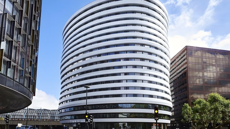 El moderno rascacielos del DLD College London con varios pisos y grandes ventanas se ve frente a un cielo azul claro.