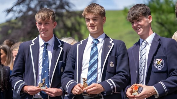 Tres estudiantes en uniformes escolares están juntos en un prado verde al aire libre en el campus de la Dollar Academy.