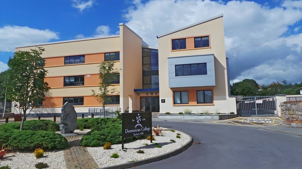 El moderno edificio del Dominican College Galway con un jardín delantero y una escultura frente a un cielo azul.