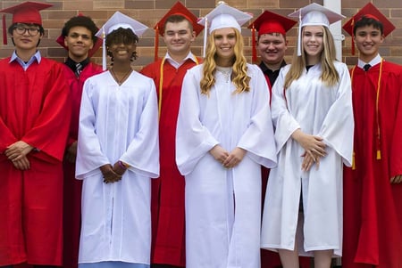 Un grupo de graduadas y graduados de la Dominion Academy of Dayton está frente a una pared de ladrillos celebrando su graduación.