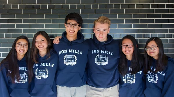 Un grupo de estudiantes del Don Mills Collegiate Institute lleva sudaderas azules con la inscripción Don Mills frente a una pared de azulejos.