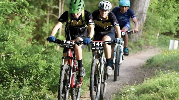 Tres ciclistas recorren un sendero forestal en el terreno de la Donahies Community School.