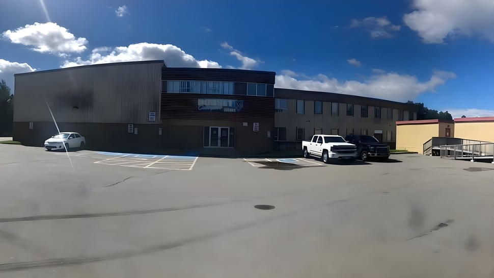 El moderno edificio de varios pisos con fachada de vidrio en el campus de Dorset Collegiate está rodeado de un estacionamiento pavimentado.