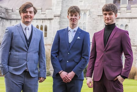 Tres estudiantes en ropa formal están de pie frente a un edificio histórico en el campus de la Douglas Community School.