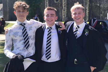 Tres estudiantes en uniformes escolares están afuera en el campus del Dover College y se ríen.