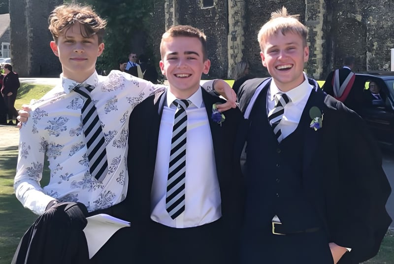 Tres estudiantes en uniformes escolares están afuera en el campus del Dover College y se ríen.