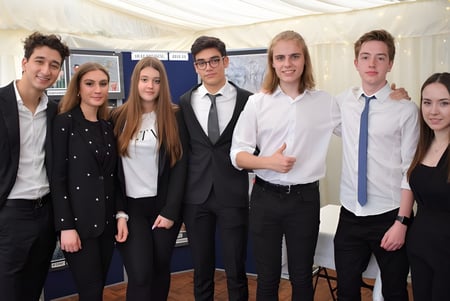 Un grupo de estudiantes en ropa formal posan frente a una carpa blanca en el campus de D'Overbroeck's College.