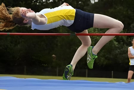 Una estudiante de la Downe House School salta en el salto de altura con un fondo verde.