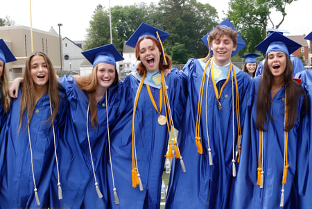 Un grupo de graduados del Downingtown Area School District está al aire libre en togas de graduación azules y amarillas.