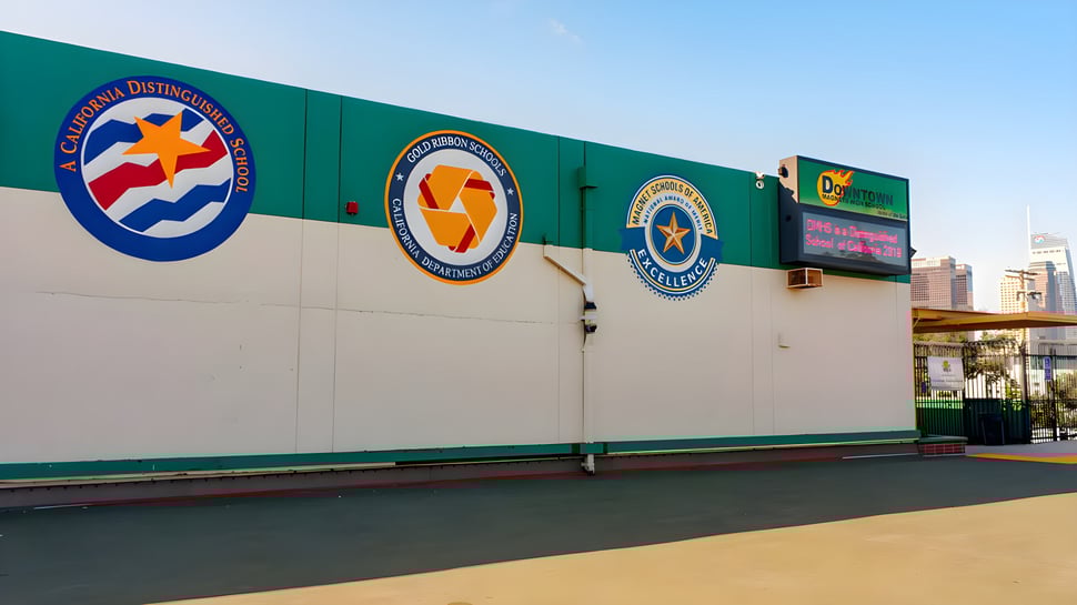 La pared verde con logotipos coloridos se encuentra en el campus de la Downtown Magnet High School frente a la vista de la ciudad.