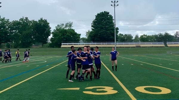 Un grupo de estudiantes de la Dr. G.W. Williams Secondary School se reúne en un campo de deportes junto a un estadio.