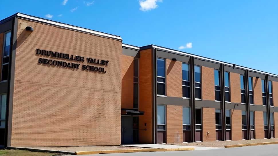 El gran edificio de ladrillo de la Drumheller Valley Secondary School se encuentra bajo un cielo azul nublado.