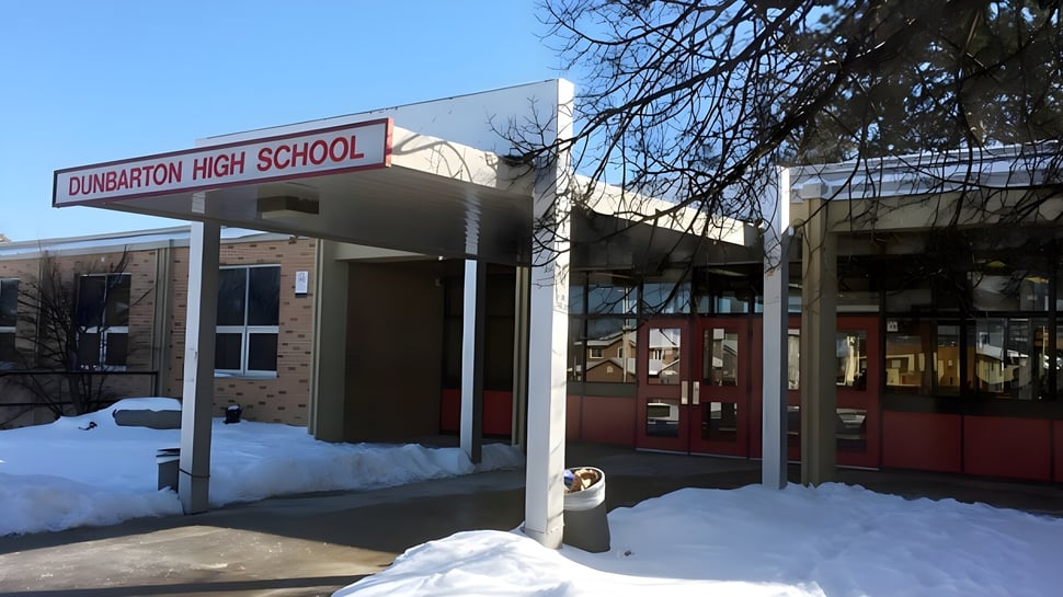 La entrada de la Dunbarton High School muestra un edificio de ladrillo con un letrero frente a árboles cubiertos de nieve.