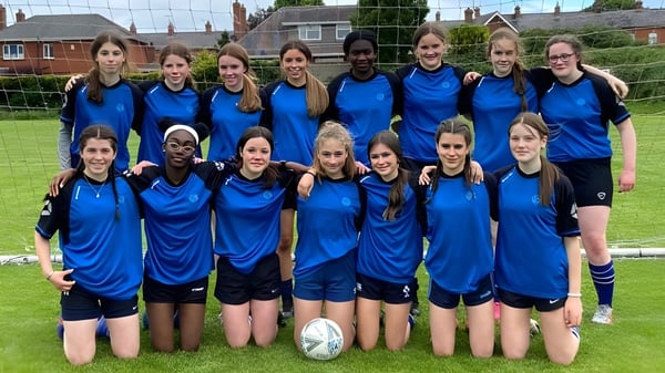 Un grupo de alumnas de la Dundalk Grammar School está reunido en una pradera frente a edificios y árboles.