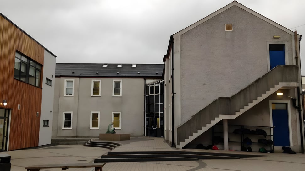 Se puede ver el edificio de varios pisos de la Dundalk Grammar School con fachada gris y una puerta de entrada azul en primer plano.