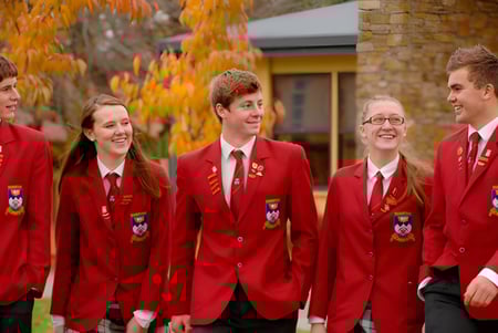 Un grupo de alumnas y alumnos de la Dunstan High School lleva uniformes rojos frente a un edificio con colorido follaje de otoño.