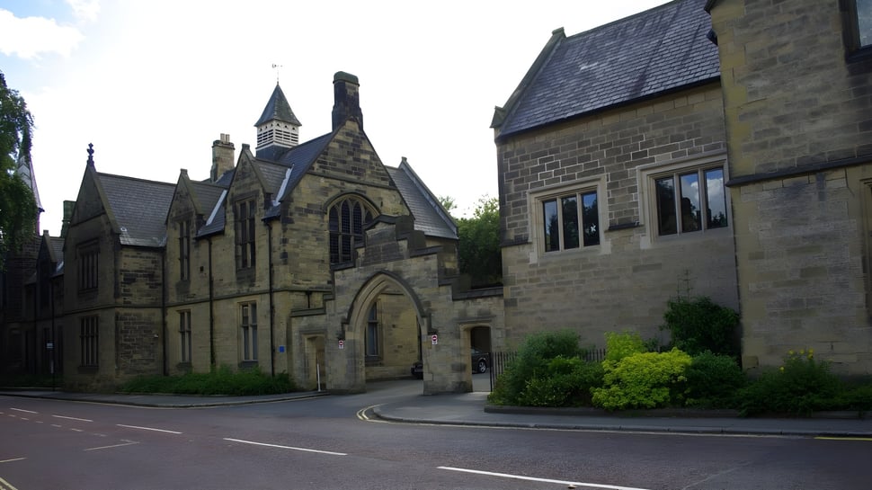 El histórico edificio de piedra principal con una alta torre y rica arquitectura decorada de la Durham School está rodeado de árboles.
