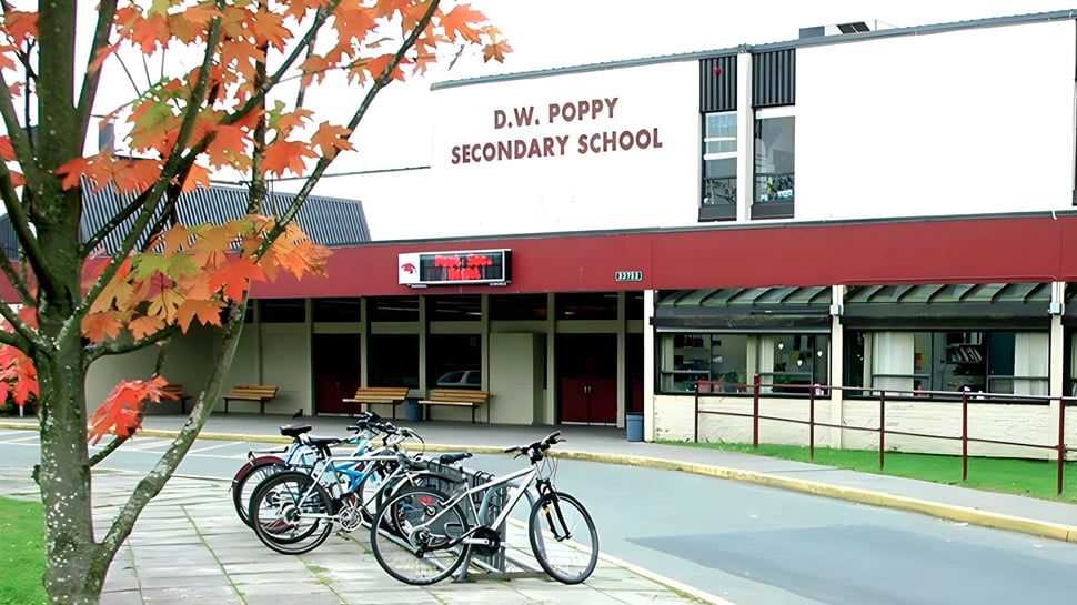El edificio de D.W. Poppy Secondary School se ve en otoño con hojas de colores y bicicletas aparcadas delante.