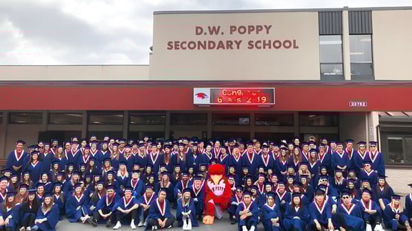 Un grupo de estudiantes está frente al edificio de D.W. Poppy Secondary School.