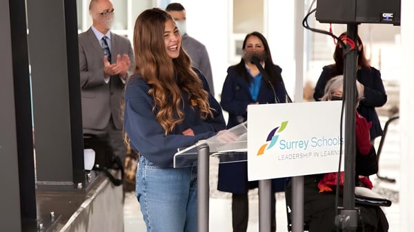Un grupo de personas está frente a un cartel que dice Surrey Service en el terreno de la Earl Marriott Secondary School.