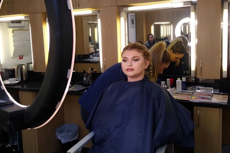 Una mujer con cabello rubio está frente a un espejo en el salón del East Sussex College Eastbourne.