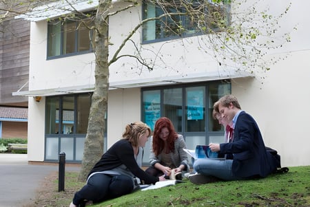 Un grupo de estudiantes del East Sussex College Lewes está sentado en el césped frente a un edificio y conversando.