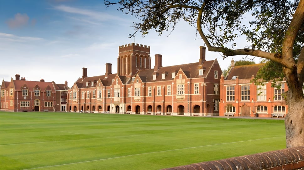 El histórico edificio de ladrillo con torres del Eastbourne College se encuentra frente a un césped verde y un gran árbol.