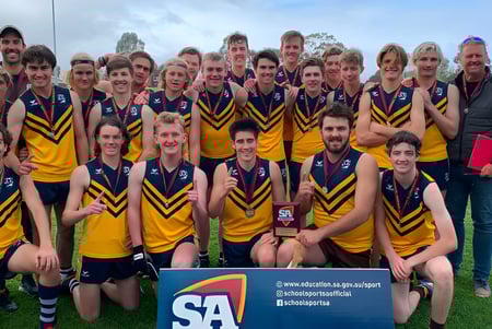 Un grupo de estudiantes de la Eastern Fleurieu R-12 posan como equipo deportivo en un campo con montañas de fondo.