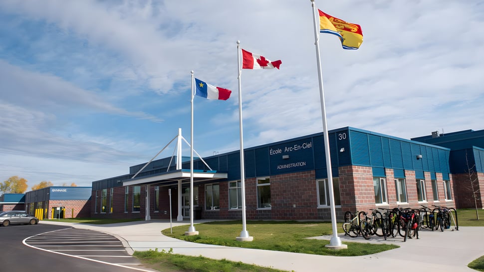 El edificio de École Arc-en-ciel muestra las banderas de Canadá y España frente a un área pavimentada con aparcamientos para bicicletas.