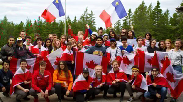 Un grupo de estudiantes de la École Aux quatre vents sostiene banderas canadienses y de la UE en un paisaje boscoso.