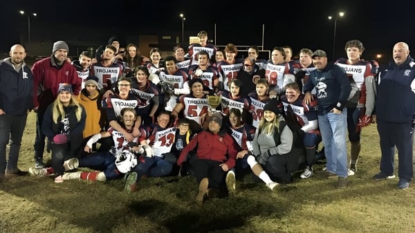 Un gran grupo de estudiantes de la École Camrose Composite High School se reúne por la noche en un campo con camisetas y carteles.