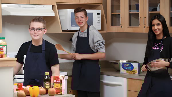 Tres alumnos de la École Dansereau Meadows School están en la cocina de la escuela preparando alimentos.